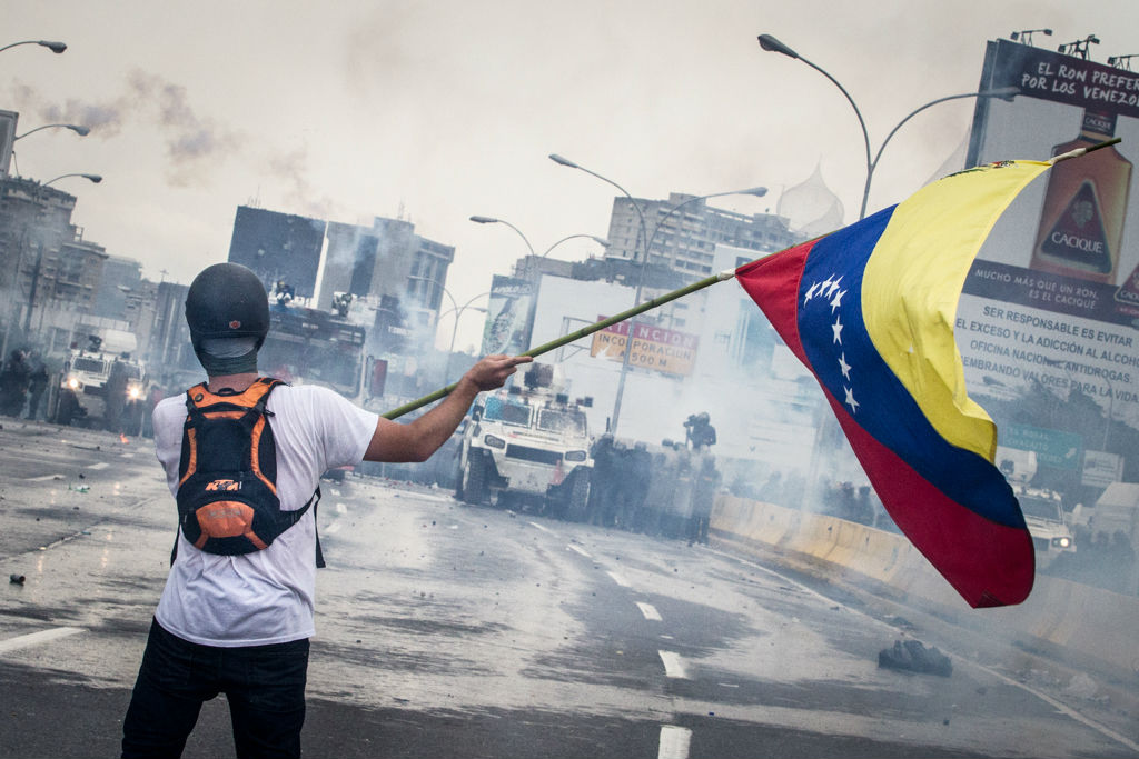 Manifestante esgrime una bandera frente a represión del régimen chavista. (Foto: Leo Álvarez)